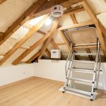 Quels détecteurs choisir pour prévenir un incendie de VMC à la maison ? Combles propres et bien éclairés d’une maison française, avec un caisson de VMC, un détecteur de chaleur au plafond et un accès sécurisé par échelle escamotable avec rampe.